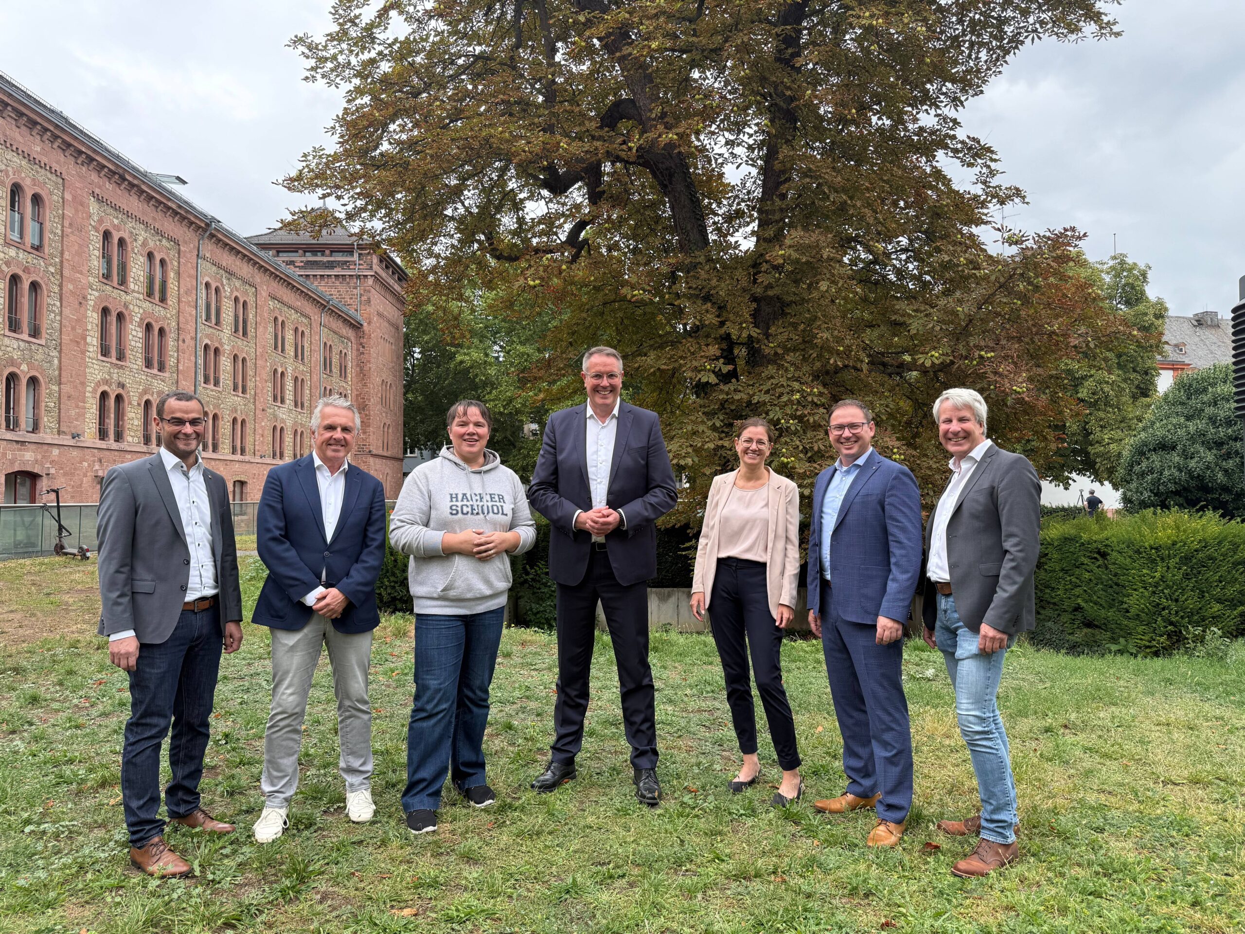 Ein Gruppenbild vor einem Baum mit dem MInisterpräsidenten Alexander Schweitzer in der Mitte und Vertretern der Hacker School, des Vereins MINTeinander Worms e. V. und der Hochschule links und rechts von ihm aufgestellt.